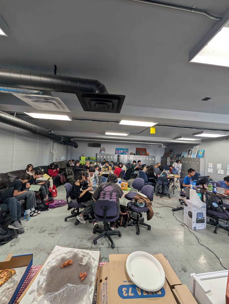 A packed room of teens coding at round tables