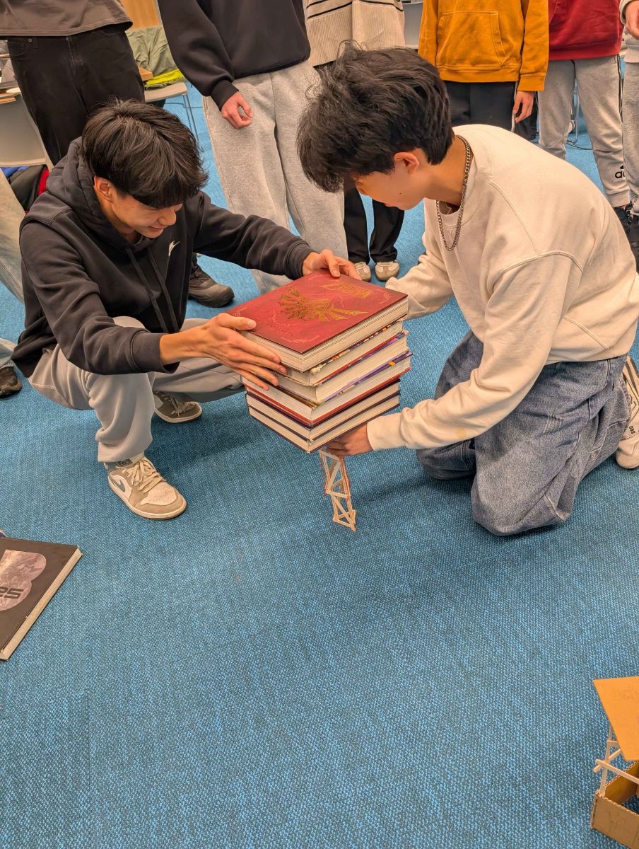 Two students stacking books on a popsicle-stick tower to test its strength