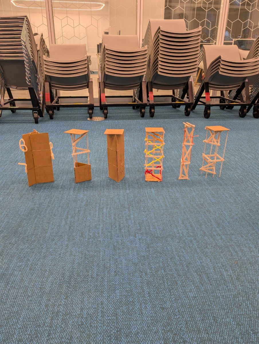 Finished popsicle-stick and cardboard towers lined up on the floor