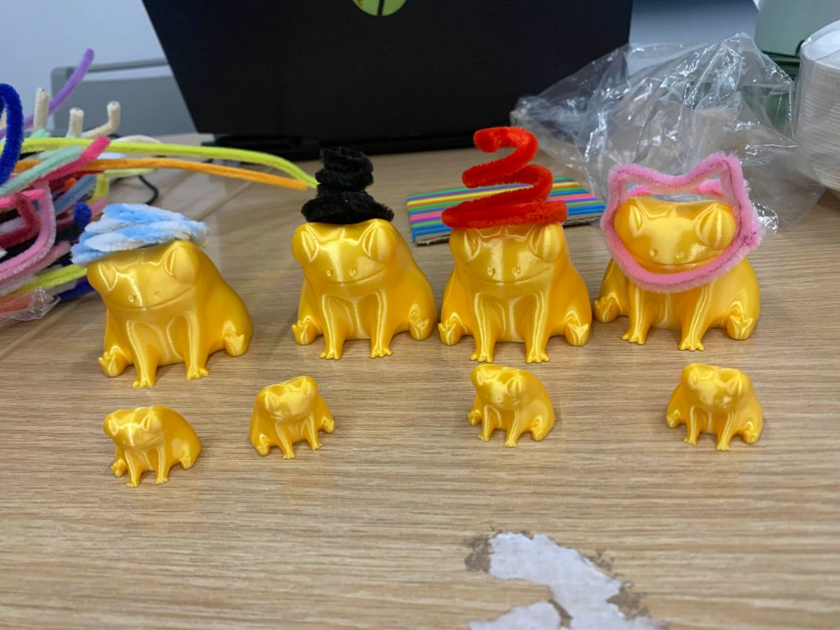 A row of gold 3D-printed frogs wearing pipe-cleaner hats