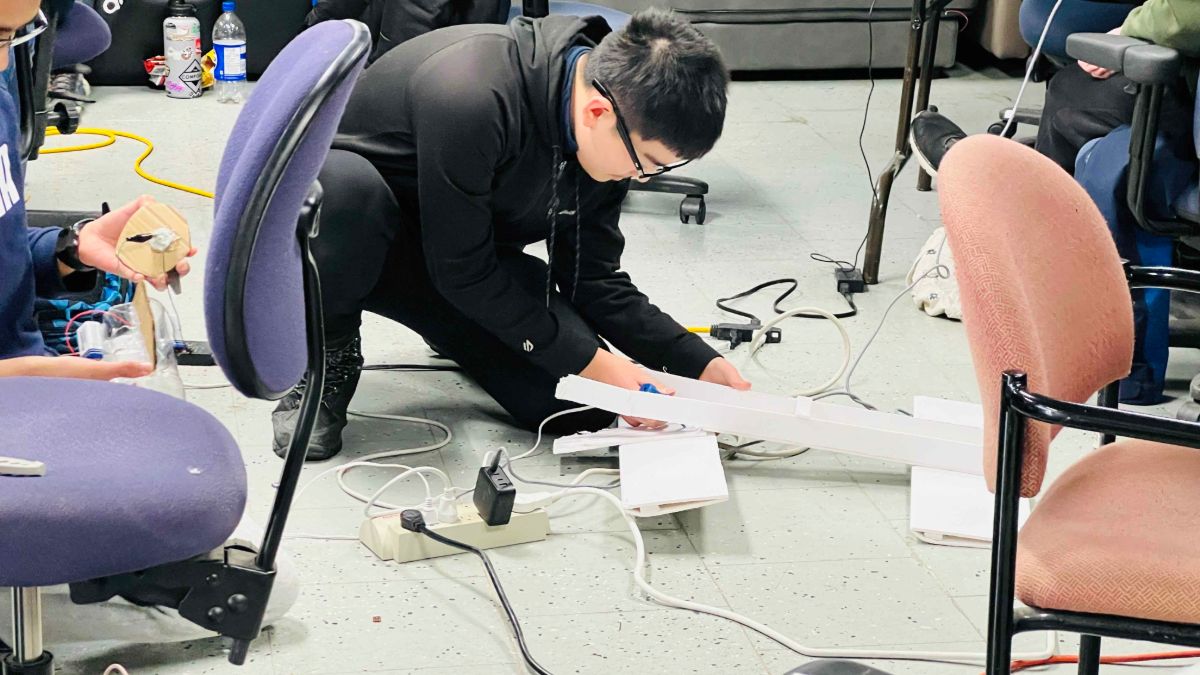 A student kneeling on the floor building a foam-board project