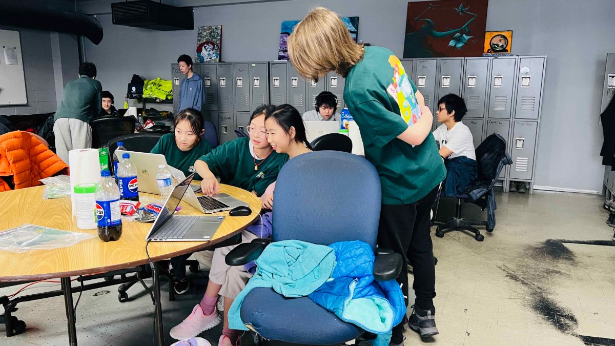 A mentor helping three students at their laptops